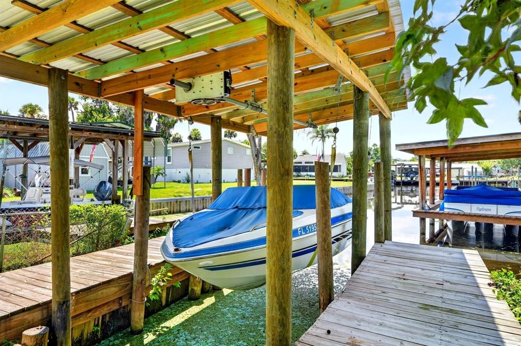 A boat lift with a covered slip sits over a canal next to a wooden dock — 55707 JAMIE DRIVE, ASTOR, FL