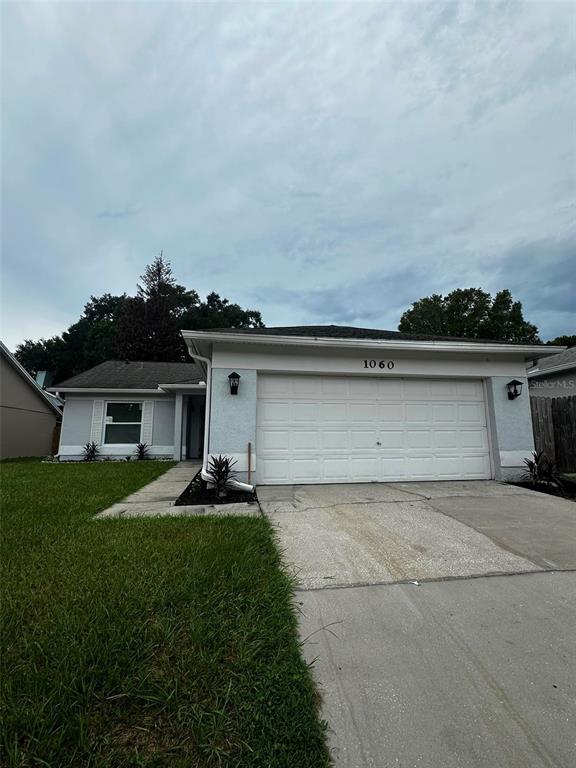 A single-story house with a white garage door, light-colored stucco siding, and a concrete driveway — 1060 DEES DRIVE, OVIEDO, FL