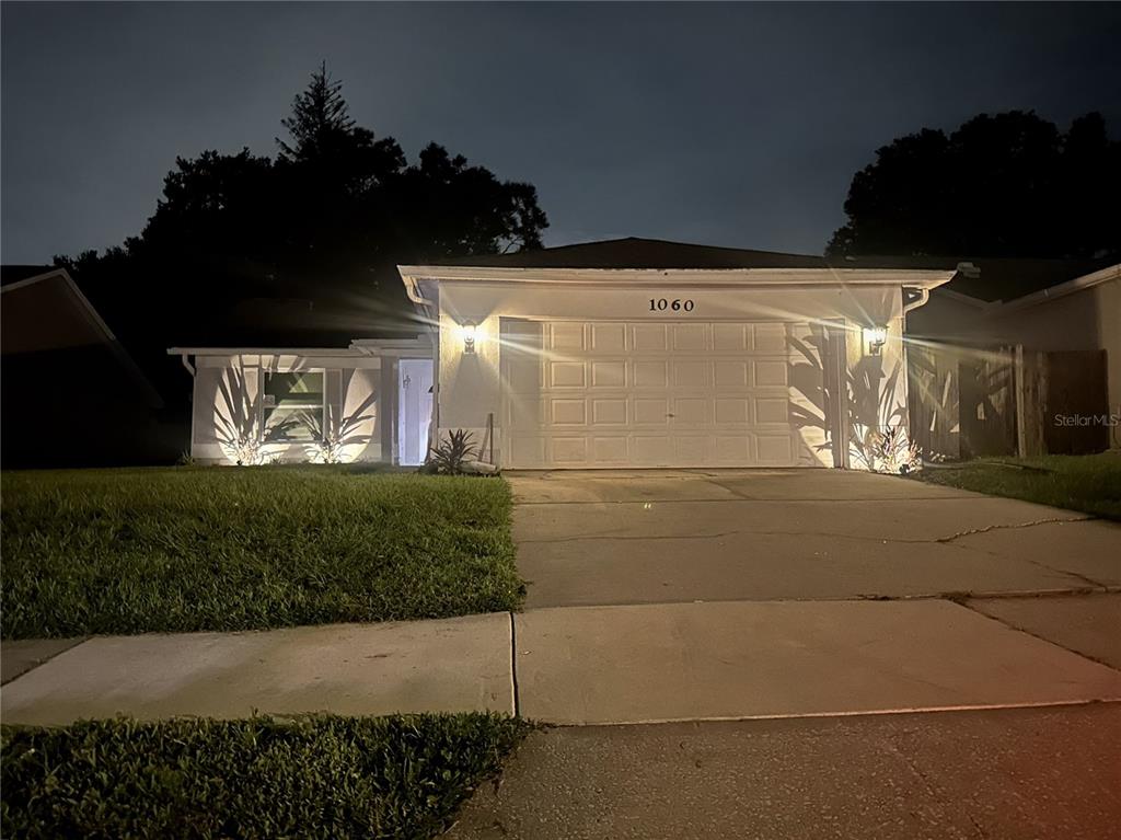 A single-story house with a white exterior, a garage, and illuminated landscaping at night — 1060 DEES DRIVE, OVIEDO, FL
