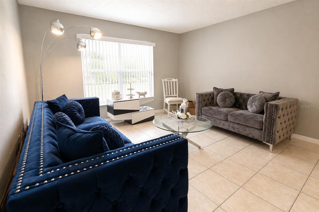 A living room features a blue velvet sofa, a grey tufted sofa, and tile flooring — 1807 MICHIGAN AVENUE UNIT B, KISSIMMEE, FL