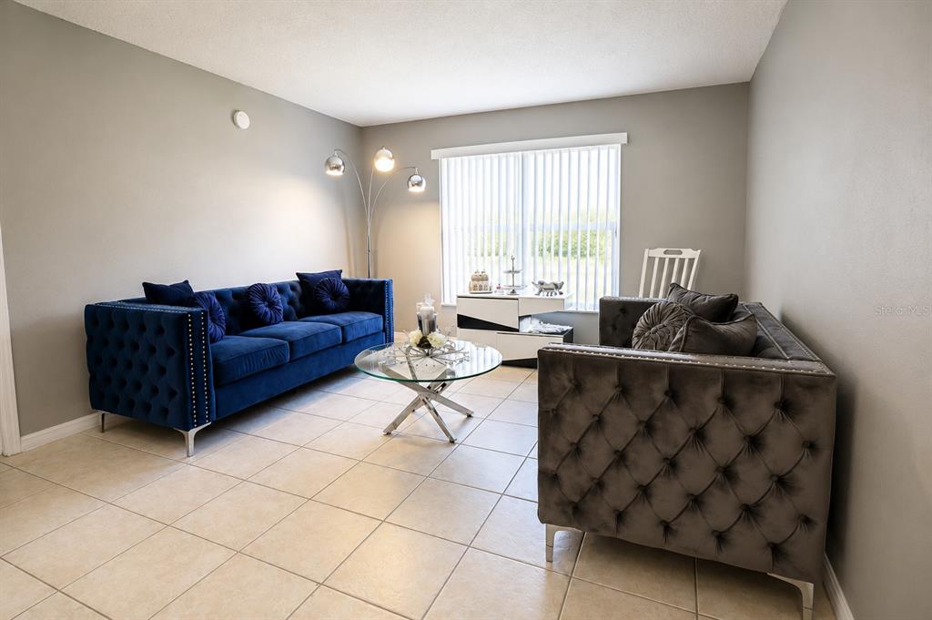 A living room features a blue velvet sofa, a grey tufted sofa, and tile flooring — 1807 MICHIGAN AVENUE UNIT B, KISSIMMEE, FL