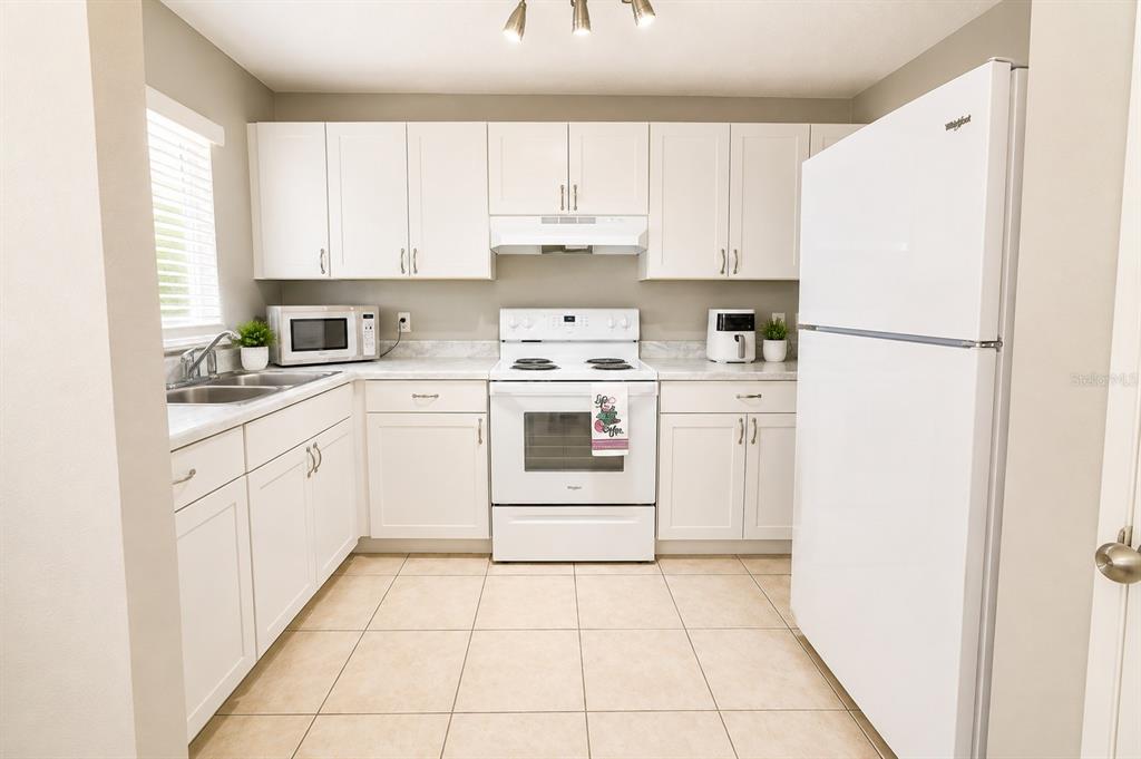 A kitchen with white cabinets, white appliances, and light-colored tile flooring — 1807 MICHIGAN AVENUE UNIT B, KISSIMMEE, FL