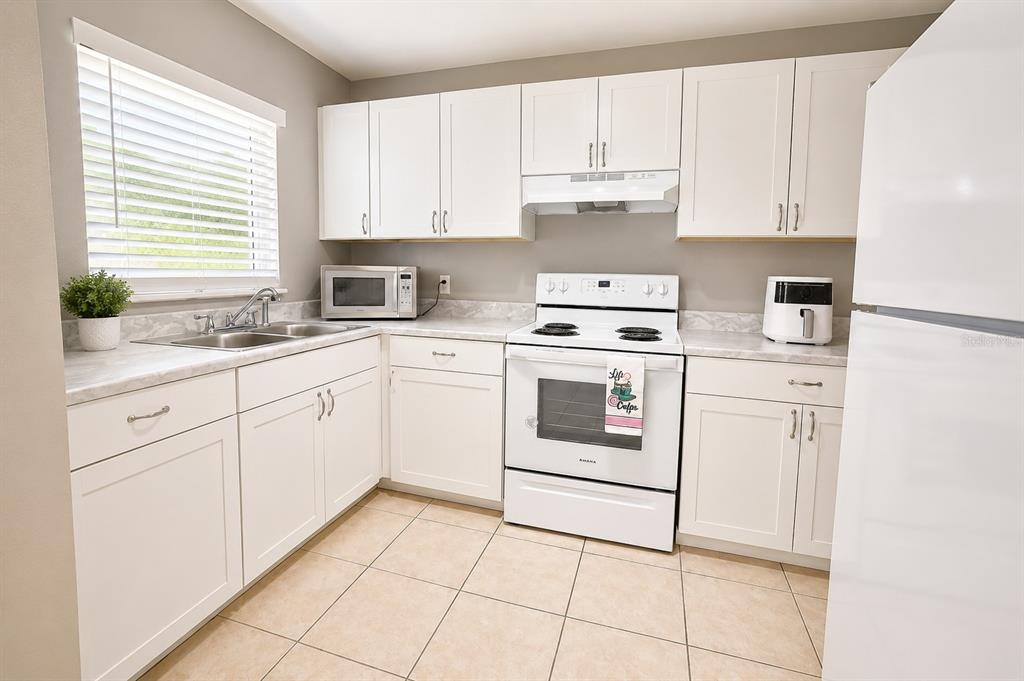 A kitchen with white cabinets, white appliances, a double sink, and light-colored tile flooring — 1807 MICHIGAN AVENUE UNIT B, KISSIMMEE, FL