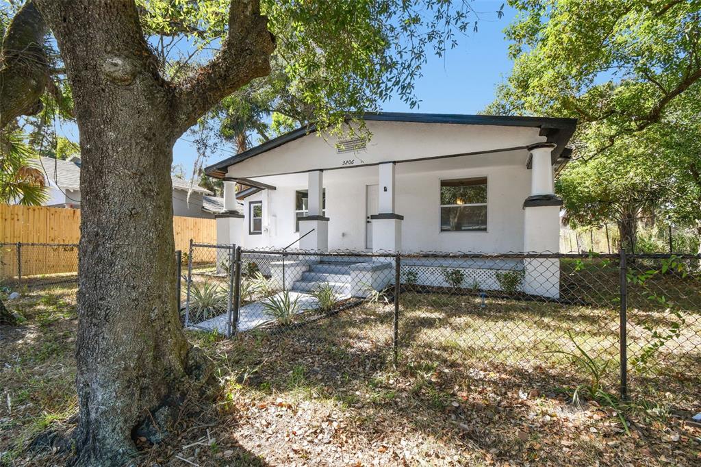 A white, single-story house with a front porch and chain-link fence stands under large trees — 3206 N 29TH STREET, TAMPA, FL
