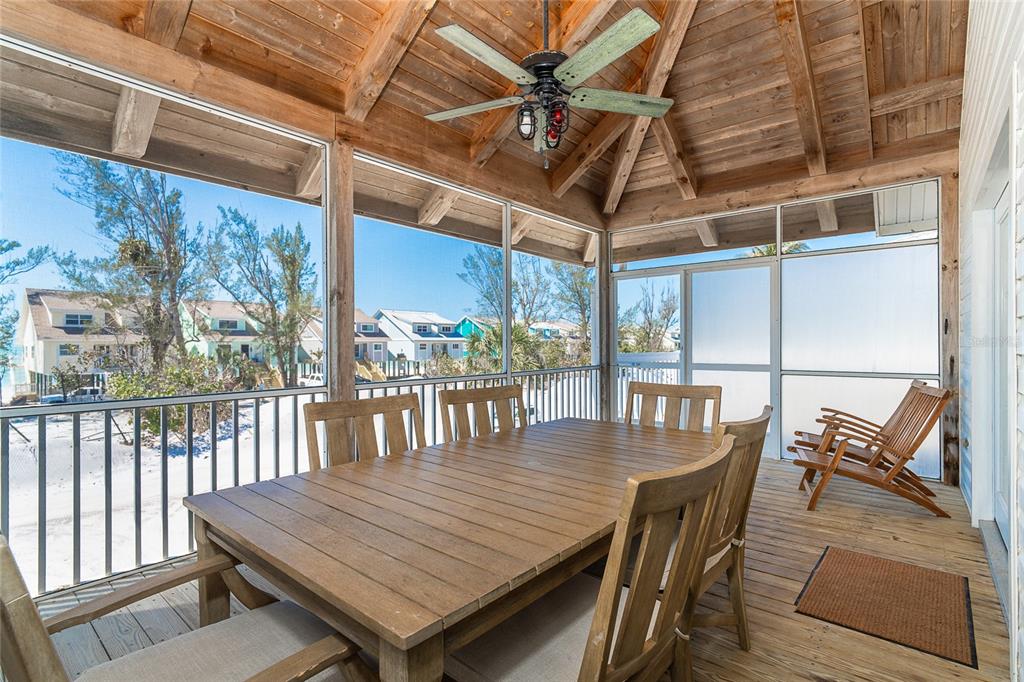 A screened-in wooden porch features a dining table, ceiling fan, and views of beach houses — 360 S GULF BOULEVARD, PLACIDA, FL