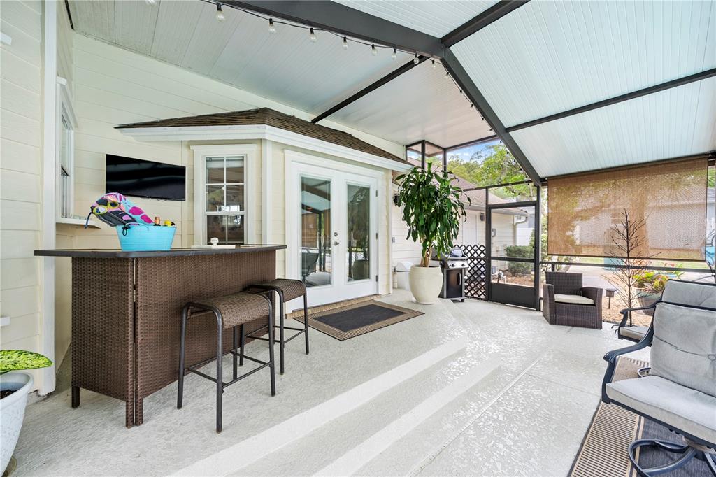 A covered patio features a bar with stools, a television, and a screened-in enclosure — 1623 SE 29TH TERRACE, OCALA, FL