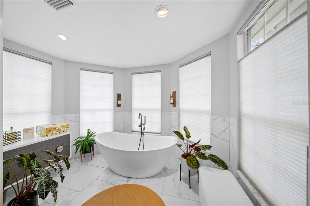 A modern bathroom features a freestanding white tub, marble-look tile floors, and large windows — 1623 SE 29TH TERRACE, OCALA, FL