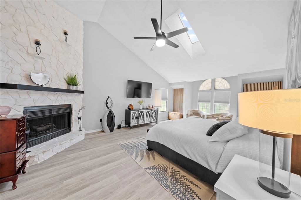 A bedroom features a stone fireplace, vaulted ceiling with a skylight, and light wood flooring — 1623 SE 29TH TERRACE, OCALA, FL