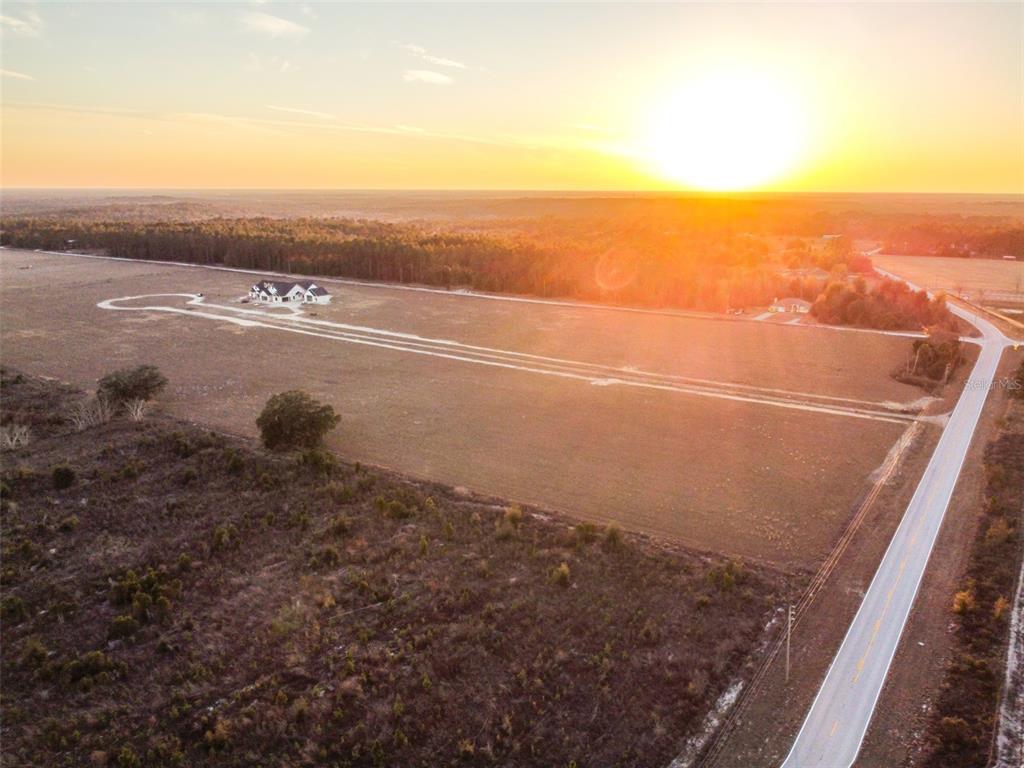 An aerial view shows a house situated on a large, open field at sunset — 4138 ROYAL SKY (LOT 10) COURT, BROOKSVILLE, FL