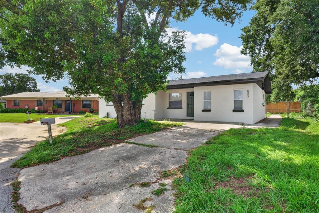 A white single-story house with a concrete driveway and a large tree in the yard — 655 TRAVIS COURT, BARTOW, FL