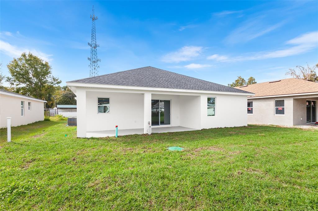 The exterior rear view of a white single-story house with a covered patio — 2519 AVENUE E SW, WINTER HAVEN, FL