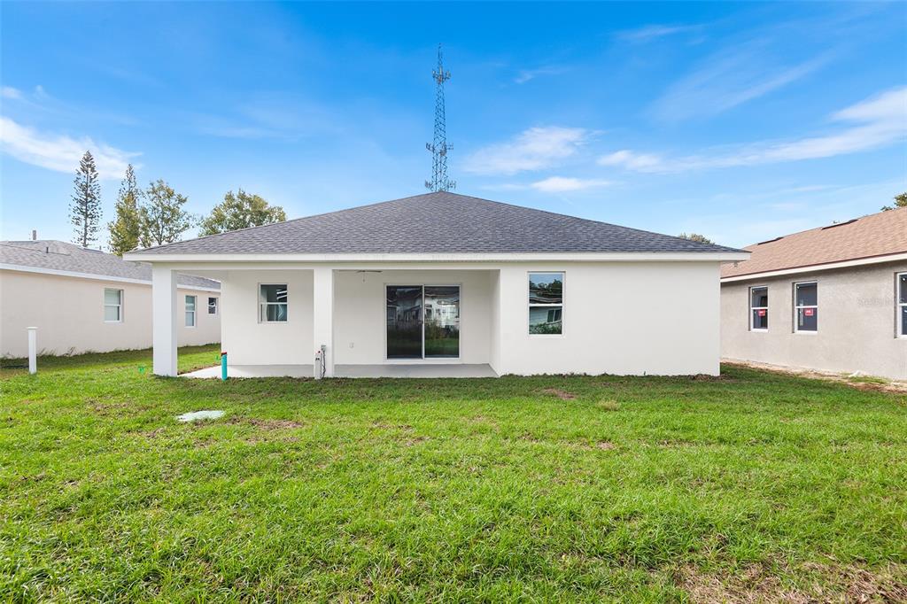 The rear exterior of a white single-story house features a covered patio and sliding glass doors — 2519 AVENUE E SW, WINTER HAVEN, FL