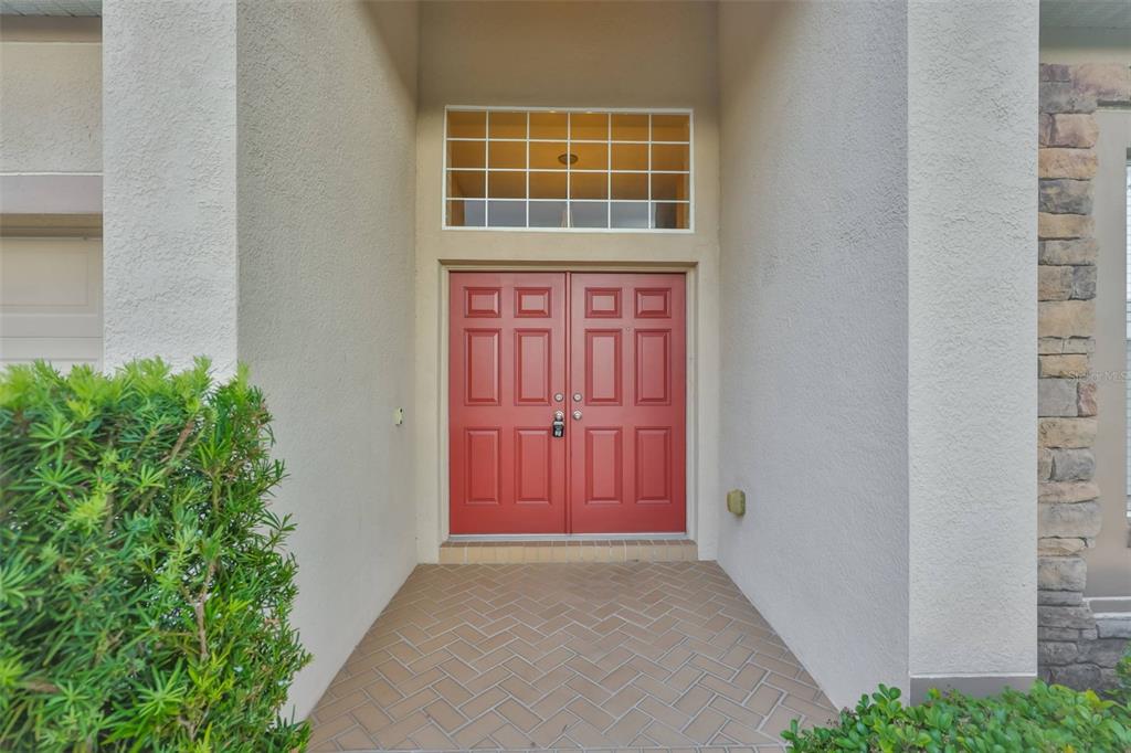 A red double front door with a transom window sits under a covered entryway — 11813 STONEWOOD GATE DRIVE, RIVERVIEW, FL