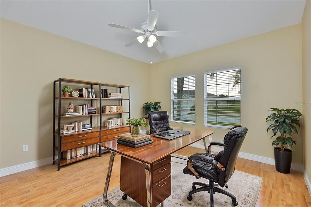 A home office with a wooden desk, black leather chairs, bookshelves, and two windows — 11813 STONEWOOD GATE DRIVE, RIVERVIEW, FL