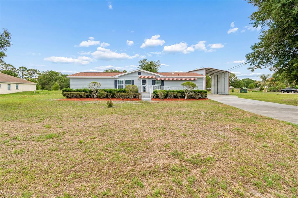 A single-story house with light blue siding, a front porch, and an attached metal carport — 3724 TACK DRIVE, WESLEY CHAPEL, FL