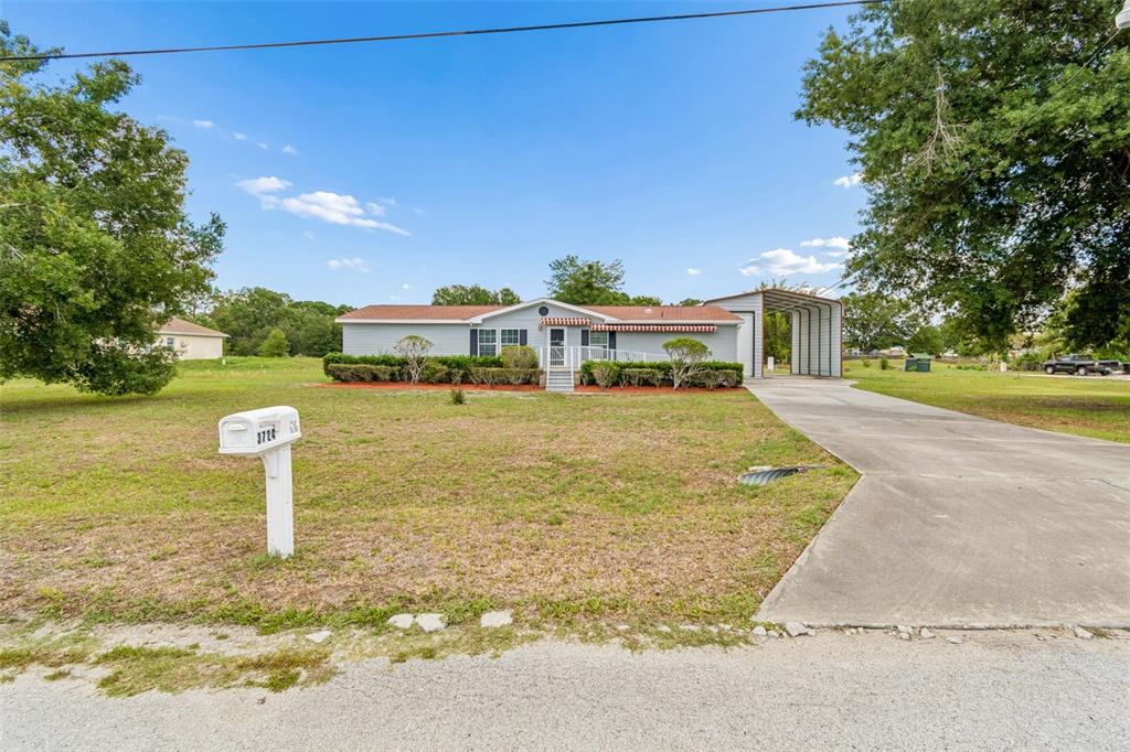A single-story house with a metal carport and a front lawn under a blue sky — 3724 TACK DRIVE, WESLEY CHAPEL, FL