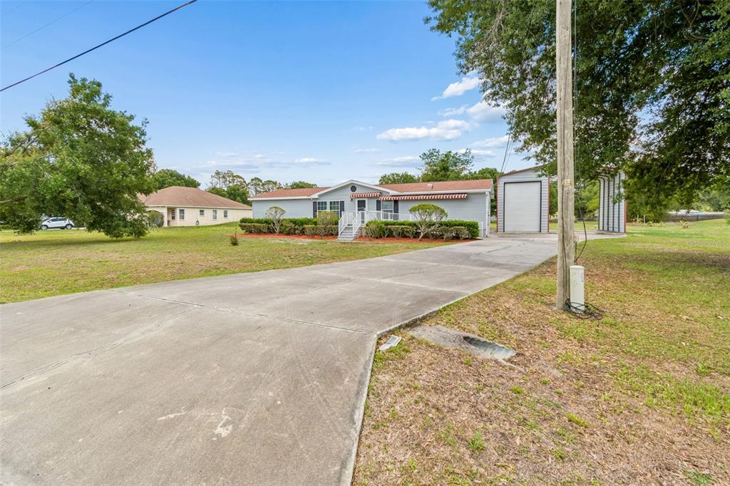 A single-story house with light blue siding, a concrete driveway, and a detached metal garage — 3724 TACK DRIVE, WESLEY CHAPEL, FL