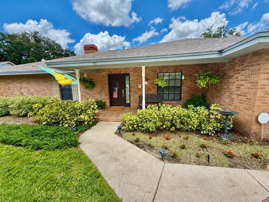 A single-story brick house features a front walkway, a covered porch, and landscaped garden beds — 411 SUMMIT CHASE DRIVE, VALRICO, FL