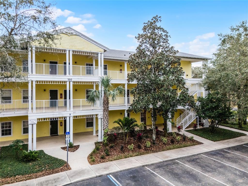 A three-story yellow apartment building features white railings, exterior staircases, and a landscaped parking area — 312 LUCAYA LOOP, DAVENPORT, FL