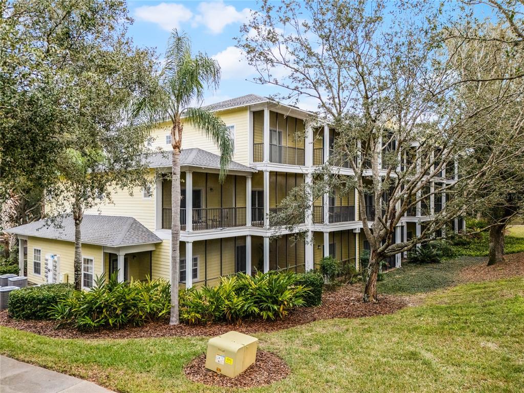 A three-story yellow apartment building with screened-in balconies and surrounding trees and landscaping — 312 LUCAYA LOOP, DAVENPORT, FL