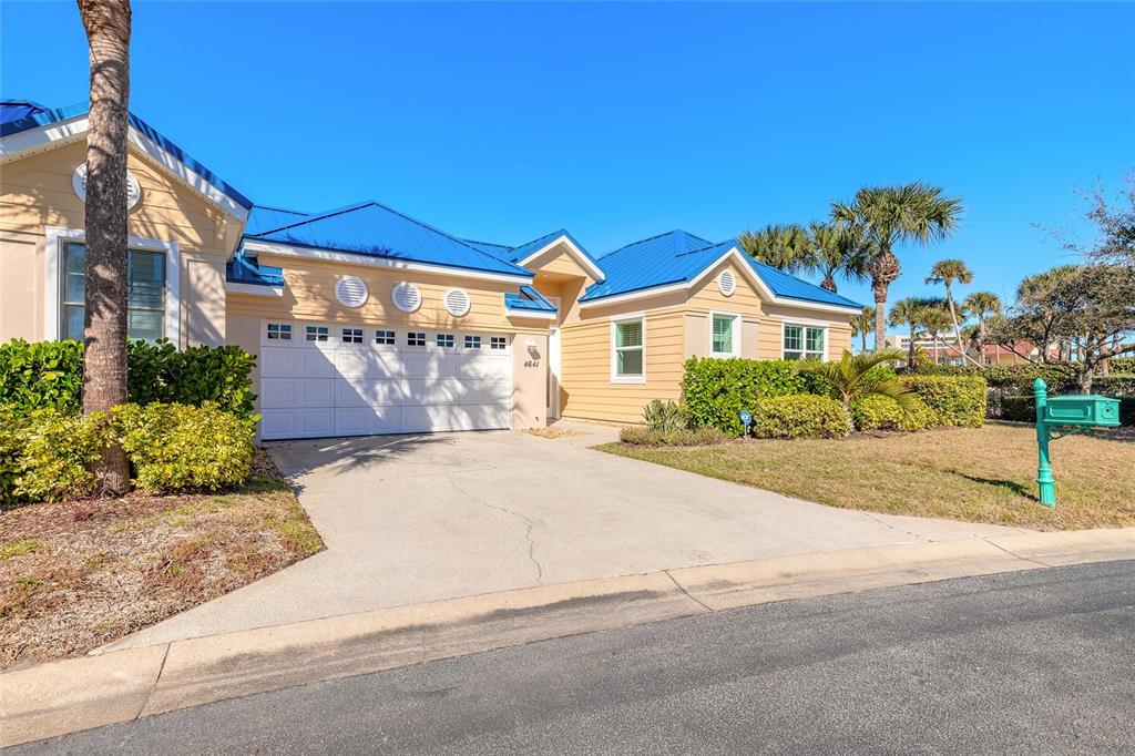 A single-story house with yellow siding, a blue metal roof, and a concrete driveway — 4641 RIVERWALK VILLAGE COURT, PONCE INLET, FL