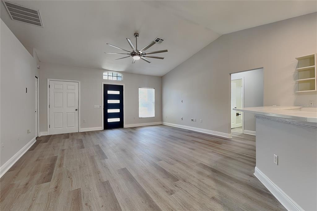 An open-concept living area features light wood-look flooring, a vaulted ceiling, and a modern front door — 4840 TIMBER WAY, ZEPHYRHILLS, FL