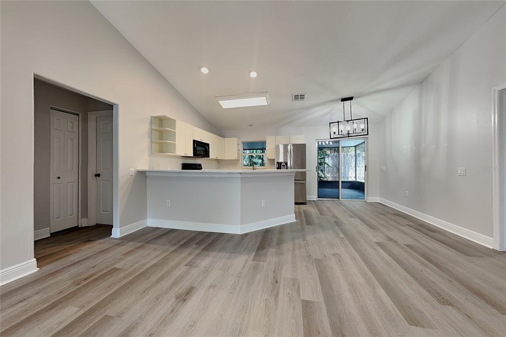A kitchen with white cabinets and a breakfast bar opens into a living area — 4840 TIMBER WAY, ZEPHYRHILLS, FL