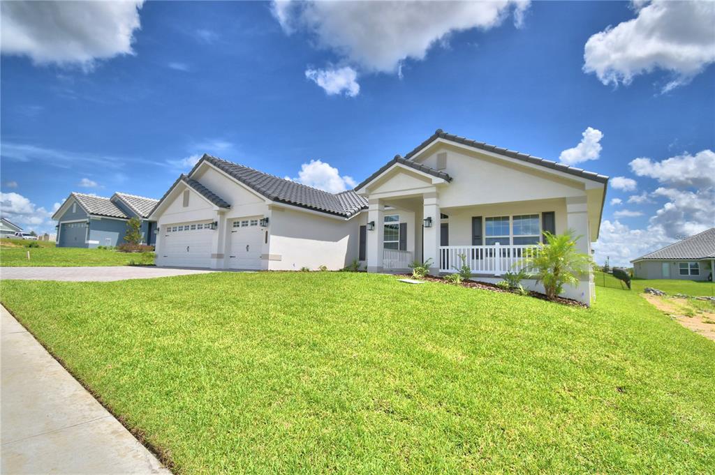 A gray house with a three-car garage and a paved driveway under a cloudy sky — 5421 WATERSIDE DRIVE, AUBURNDALE, FL