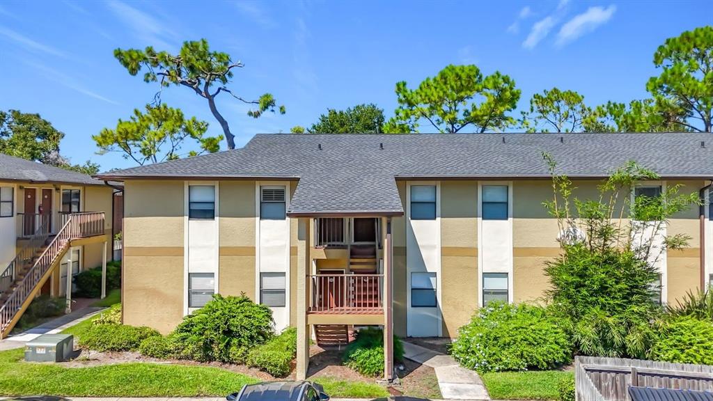 A two-story apartment building with tan stucco walls, a gray shingled roof, and exterior staircases — 10199 SAILWINDS BOULEVARD S UNIT 201, LARGO, FL