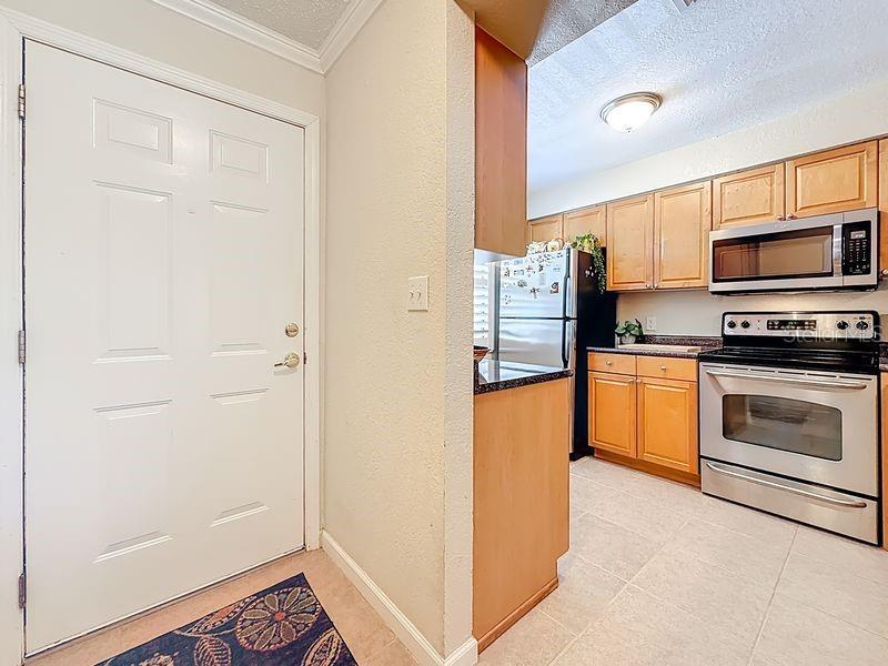 A white door opens into a kitchen featuring light wood cabinets and stainless steel appliances — 10199 SAILWINDS BOULEVARD S UNIT 201, LARGO, FL