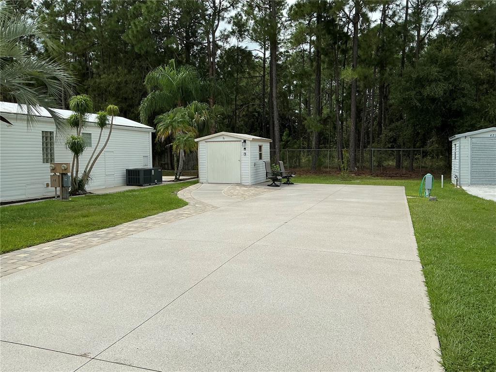 A concrete driveway leads to a small storage shed between two white mobile homes — 427 PINE LOOP, FROSTPROOF, FL