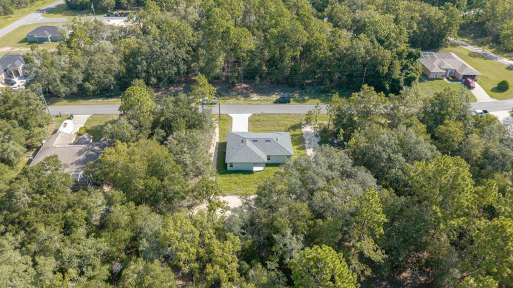 An aerial view shows a single-story house surrounded by dense trees and a paved road — 2126 W CHARLENE PLACE, DUNNELLON, FL