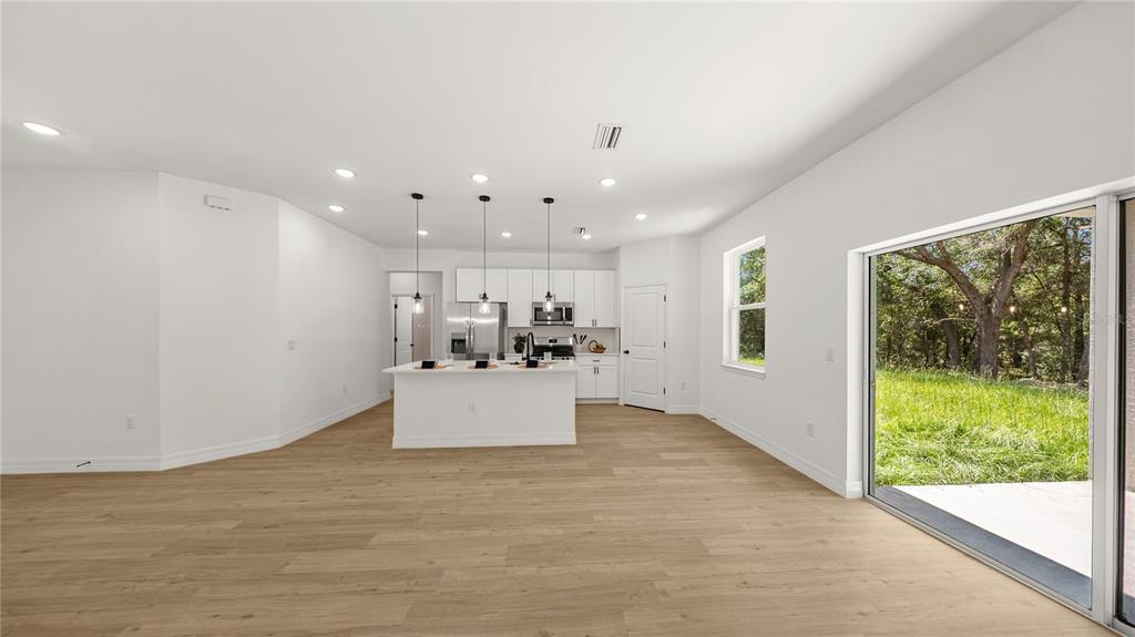 A bright, open-concept kitchen and living area features white cabinets, a central island, and sliding doors — 2126 W CHARLENE PLACE, DUNNELLON, FL