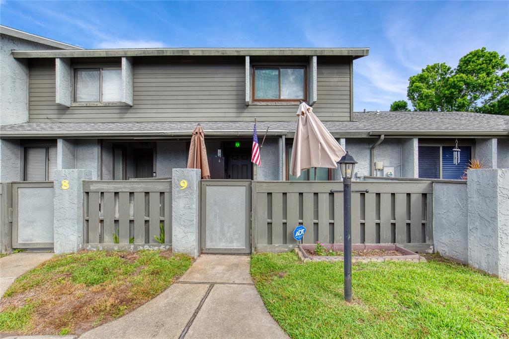 A two-story townhouse exterior features a fenced front courtyard, a walkway, and green lawn — 210 LEMON TREE LANE UNIT 9, ORMOND BEACH, FL