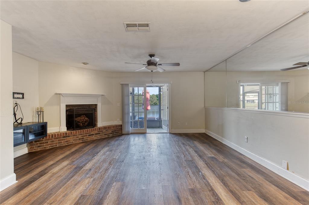 A living room with wood-look flooring, a brick fireplace, sliding glass doors, and mirrored walls — 210 LEMON TREE LANE UNIT 9, ORMOND BEACH, FL