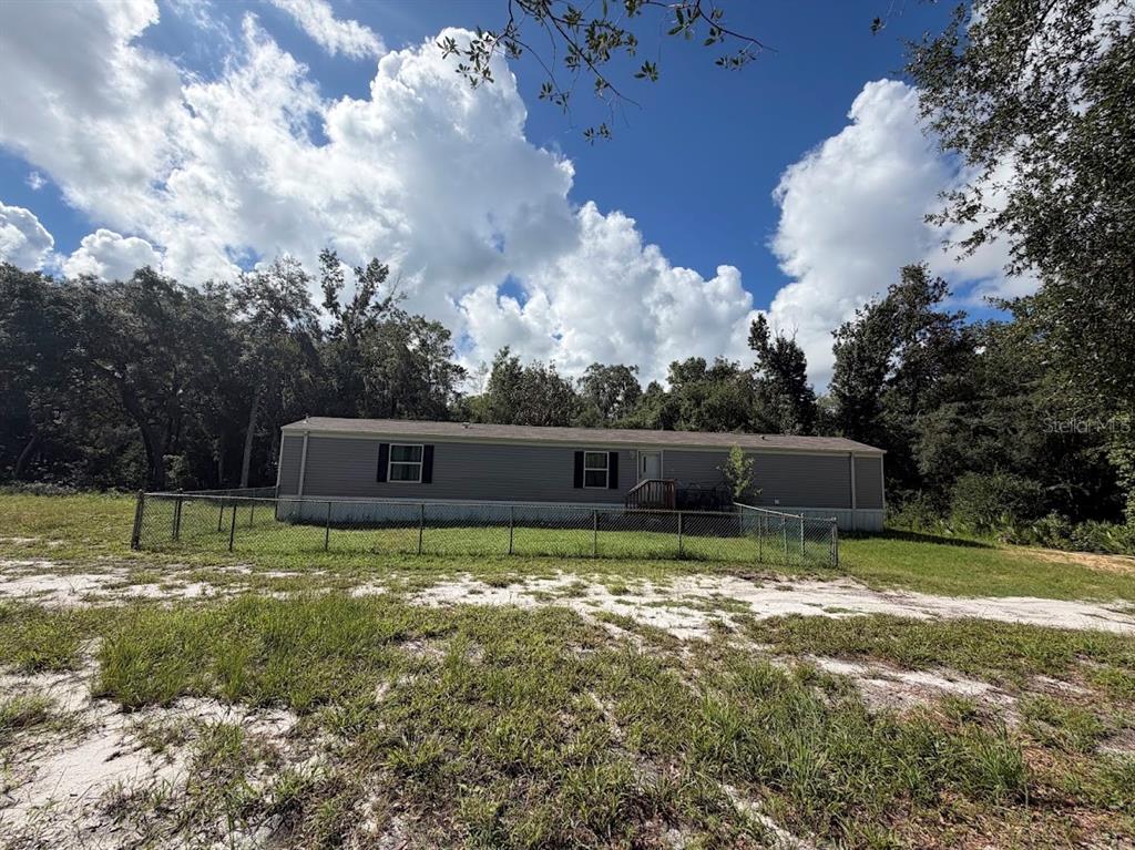 A single-story manufactured home sits on a grassy lot enclosed by a chain-link fence — 16456 NE 35TH AVENUE ROAD, CITRA, FL