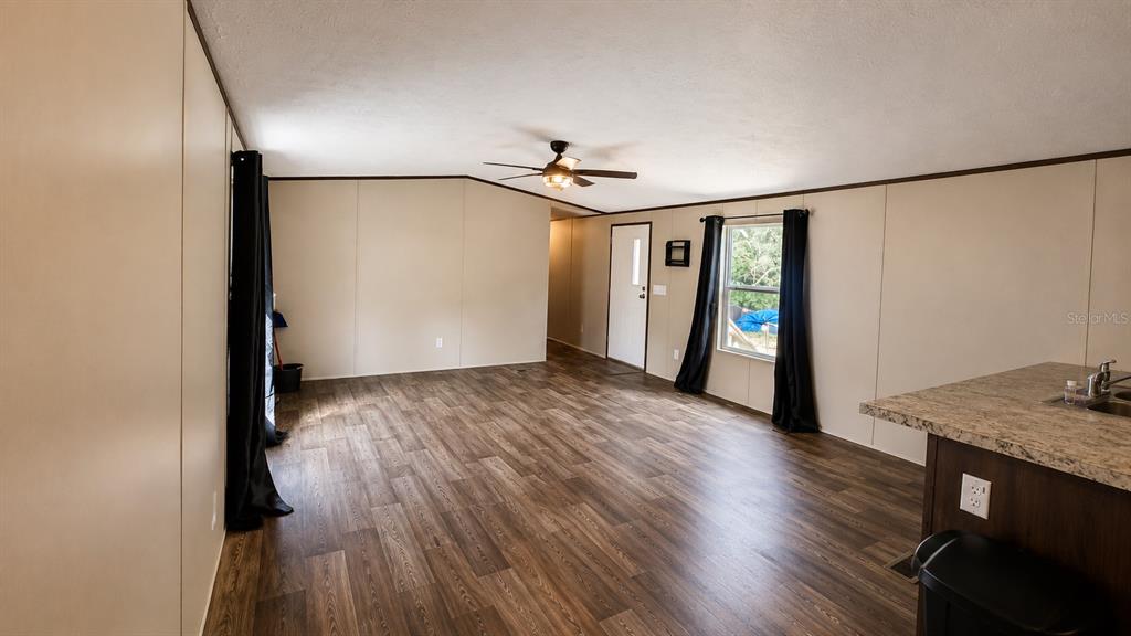 An open-concept living area features wood-look flooring, beige walls, a ceiling fan, and a kitchen island — 16456 NE 35TH AVENUE ROAD, CITRA, FL