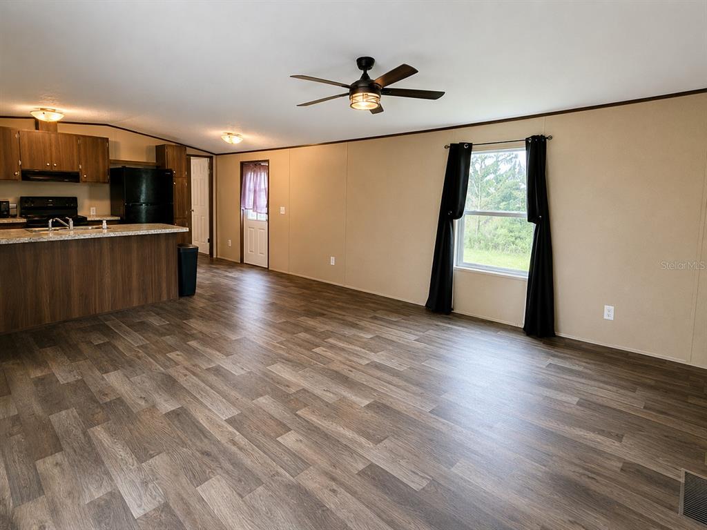 An open-concept kitchen and living area features wood-look flooring, dark cabinets, and a ceiling fan — 16456 NE 35TH AVENUE ROAD, CITRA, FL