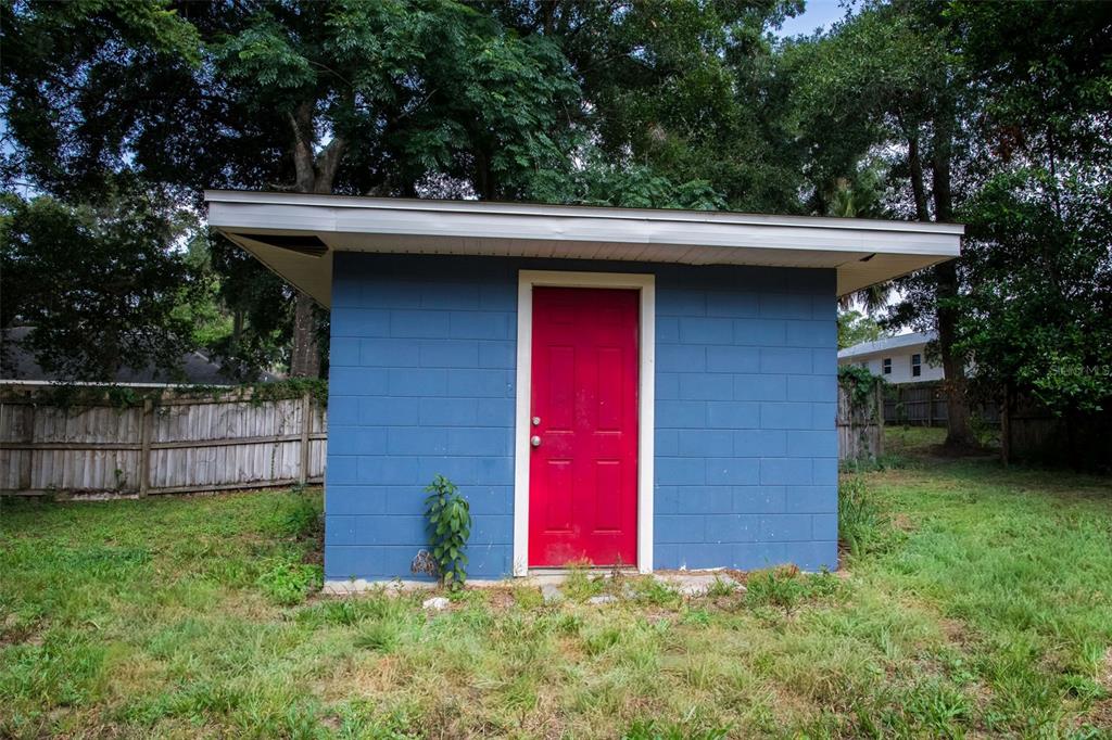 A blue concrete block shed with a bright red door stands in a grassy yard — 900 KENTUCKY BOULEVARD, EUSTIS, FL