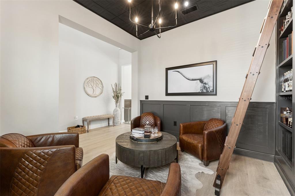 A study features leather armchairs, a round coffee table, a rolling ladder, and dark wainscoting — 16111 VOLTERRA POINT, MONTVERDE, FL