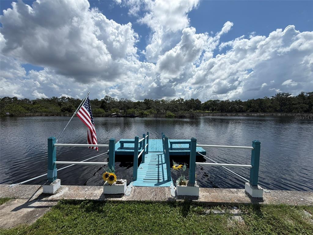 A blue wooden dock with a flag extends into a lake under a cloudy sky — 1332 FLOTILLA DRIVE, HOLIDAY, FL