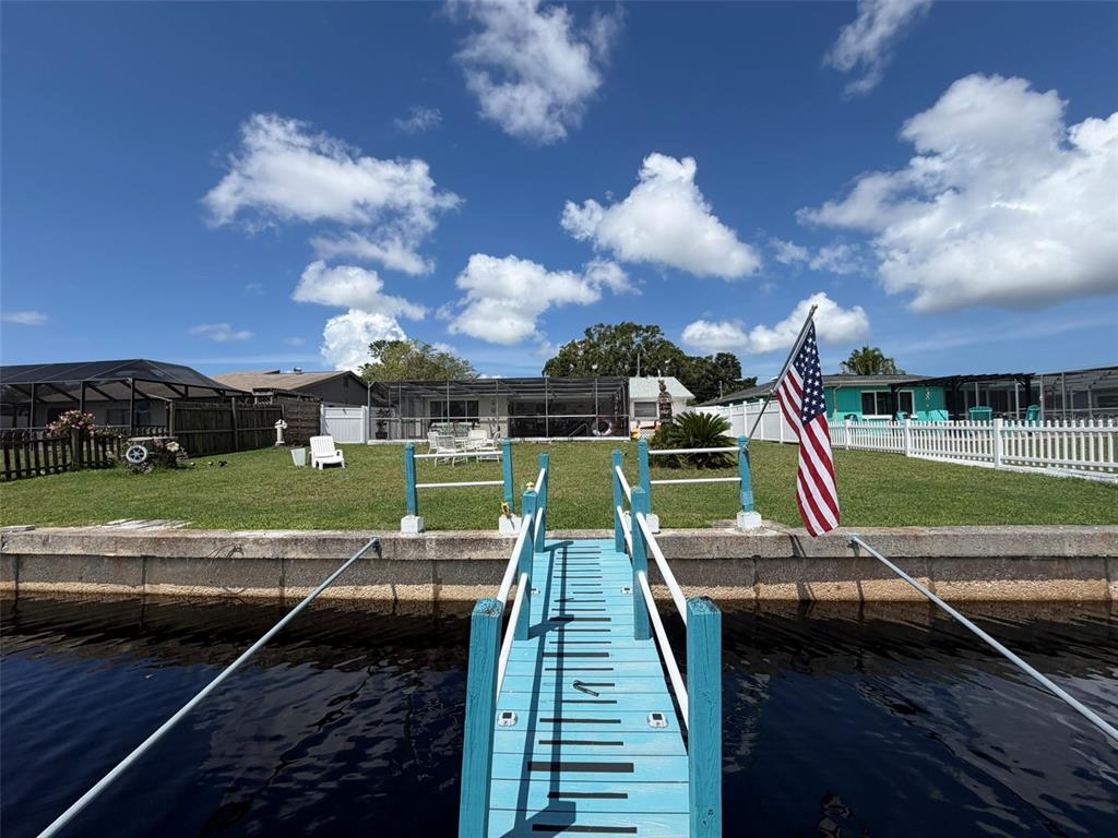A blue wooden dock leads to a grassy backyard with a house and American flag — 1332 FLOTILLA DRIVE, HOLIDAY, FL