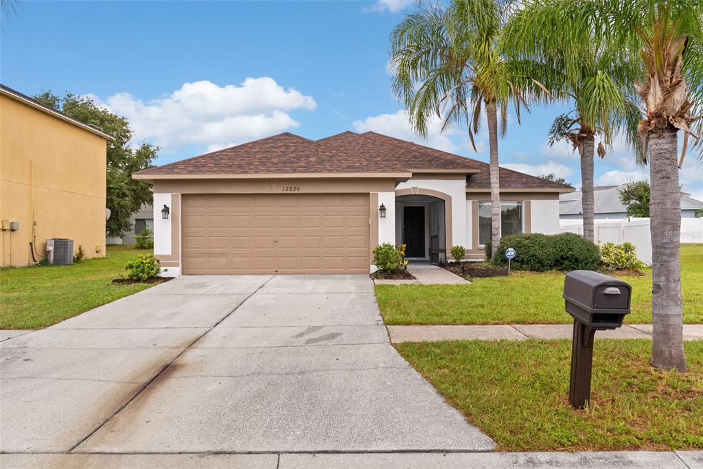 A single-story house with a tan stucco exterior, brown roof, and a two-car garage — 12826 LONGCREST DRIVE, RIVERVIEW, FL