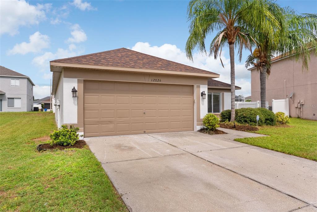 A single-story house with a tan garage door, a concrete driveway, and a palm tree — 12826 LONGCREST DRIVE, RIVERVIEW, FL