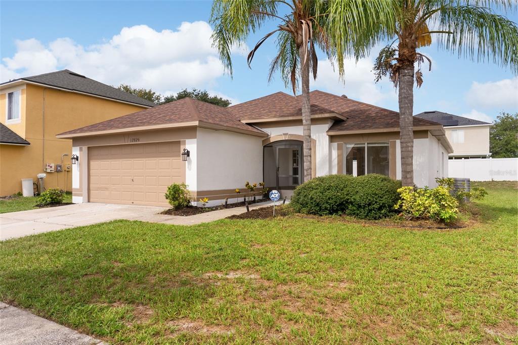 A single-story suburban house with a tan stucco exterior, brown roof, and two palm trees — 12826 LONGCREST DRIVE, RIVERVIEW, FL