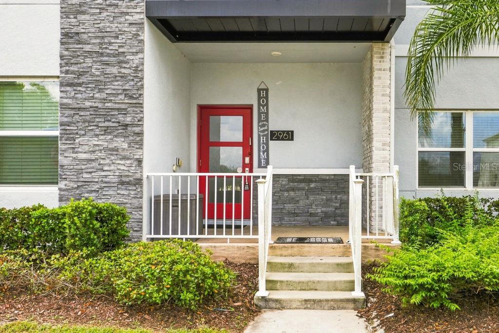 The exterior of a home features a red front door, stone siding, and a porch — 2961 SIMILE STREET, KISSIMMEE, FL