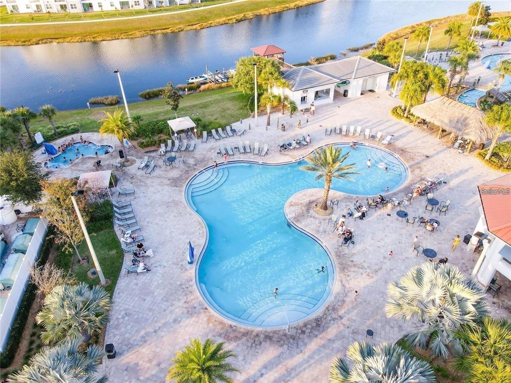 An aerial view shows a community swimming pool complex with lounge chairs and a lake — 2961 SIMILE STREET, KISSIMMEE, FL