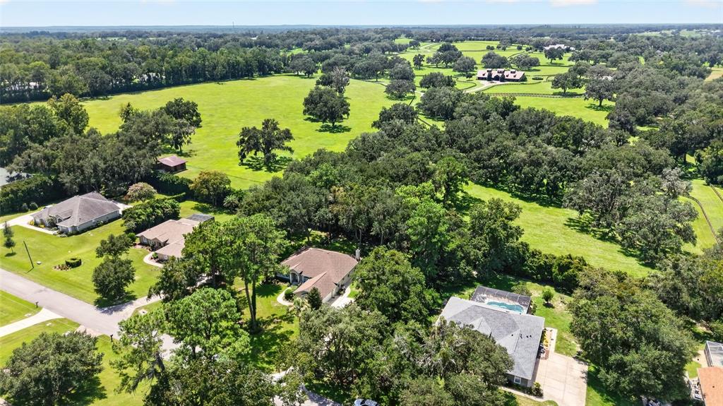 An aerial view shows several houses surrounded by large green pastures and mature oak trees — 5156 NW 82ND COURT, OCALA, FL