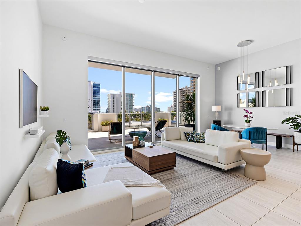 A modern living room features white sofas, a wooden coffee table, and a large balcony — 301 QUAY COMMONS UNIT 509, SARASOTA, FL