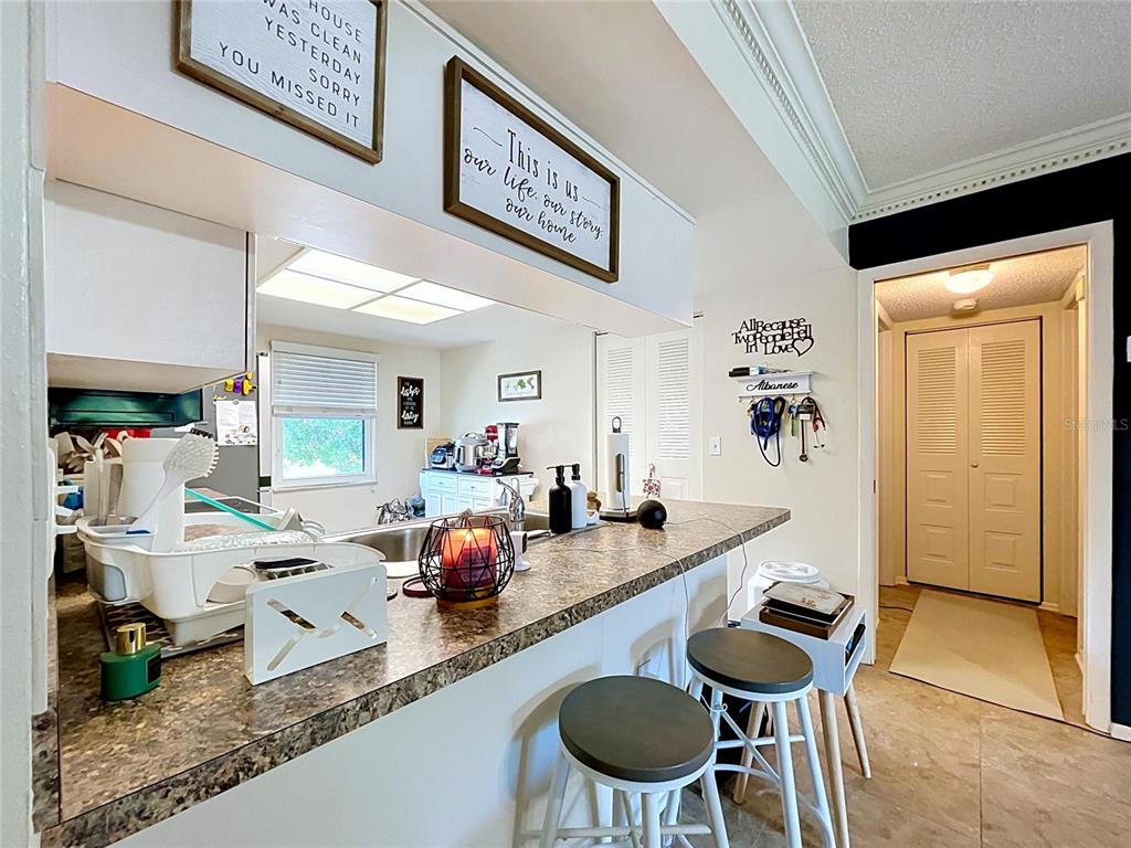 A kitchen features a breakfast bar with two stools, granite countertops, and decorative wall signs — 202 MEADOW LANE UNIT 50, OLDSMAR, FL